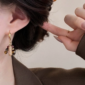 Detailed close-up of tiger eye stone puppy tassel earring with gold plating on ear model