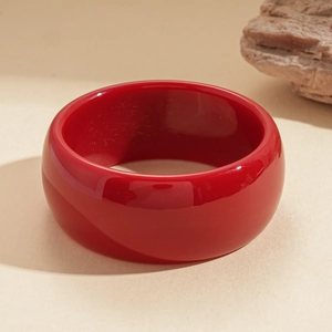 Macro shot of a chunky red resin bangle bracelet on a natural stone aesthetic background