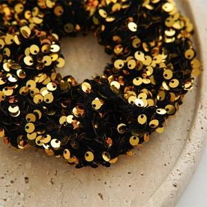 Detailed close-up of a sparkling gold sequin scrunchie with dense reflective circular accents