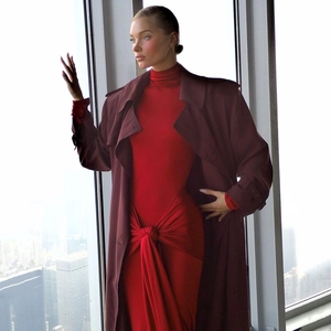 Détail d'une robe rouge moulante avec nœud à la taille et un trench-coat bordeaux long