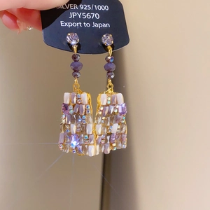 Detailed close-up of purple crystal earrings with 925 silver ear hooks and gold accents