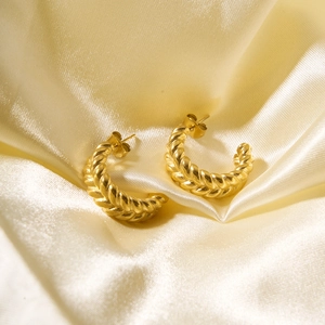 Detail of gold twisted rope hoop earrings resting on soft elegant silk fabric