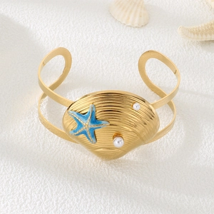 Close-up of golden shell bracelet with blue starfish and pearls on a beach background