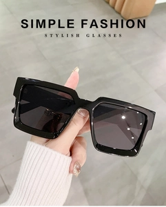 Detail of square oversized black sunglasses held by hand with simple fashion text