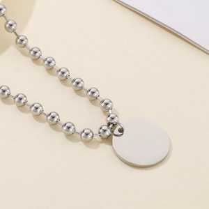 Détail du collier à pendentif disque argenté avec chaîne à boules sur fond sobre