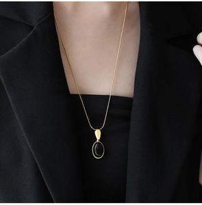 Detail of a gold snake chain necklace with an oval black resin pendant on a black blazer