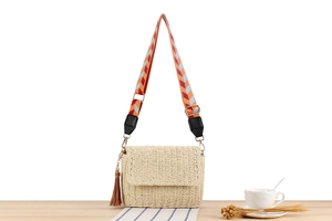 Detail of hand-woven straw crossbody bag with chevron pattern strap and leather tassel