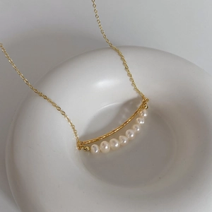 Detail of baroque freshwater pearl necklace with gold twisted bar on white ceramic