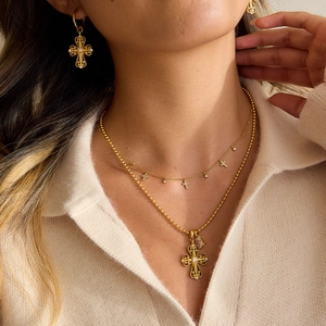 Close-up of vintage gold cross necklaces and earrings set on model with bead chain details