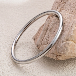 Close-up of minimalist silver stainless steel bangle resting on natural wood background
