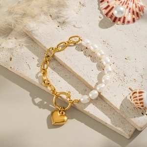 Detailaufnahme des goldenen Herz-Perlenarmbands auf einer beigen Travertin-Steinoberfläche