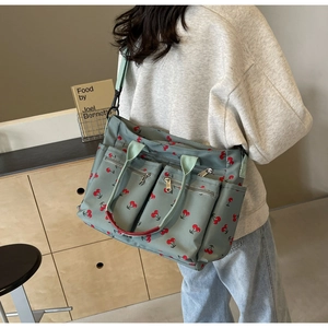 Detail of green tote bag with red cherry print featuring multiple zipper pockets