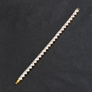 Macro shot of gold tennis chain featuring heart-shaped cubic zirconia on black background