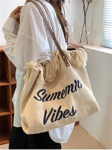 Detail of canvas tote bag with Summer Vibes embroidery, fringed edges, and leather handles