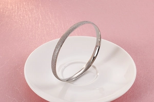 Macro shot of silver titanium bangle featuring a glittery frosted finish on white porcelain