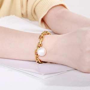 Detail of chunky gold chain bracelet with a large white pearl drop on female wrist