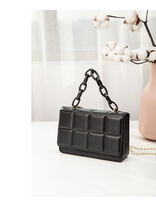 Detailed view of black quilted square bag with gold hardware and acrylic chain handle