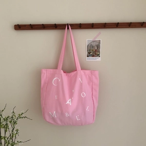 Rosafarbene Canvas-Einkaufstasche mit weißem Buchstabendruck an einer hellen Wand