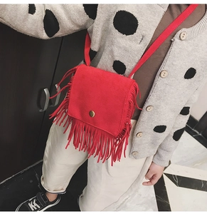 Detail of red faux suede crossbody bag featuring long fringes and circular snap closure