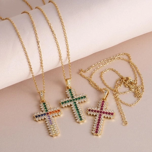 Cross necklace with gold plating and colorful zircons on a soft beige silk backdrop