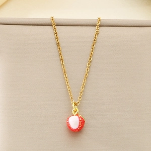 Detailed view of a gold strawberry fruit pendant necklace on a soft beige fabric background
