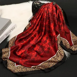 Red satin square scarf with floral and leopard patterns draped on a black quilted bag