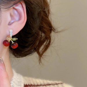 Détail des boucles d'oreilles cerise avec résine rouge et zircon vert portées à l'oreille
