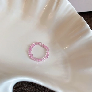 Detailed close-up of pink glass beaded elastic ring displayed on a white shell plate