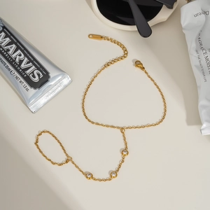 Elegant gold stainless steel finger bracelet with three clear zircons on a beige background