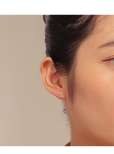 Close-up of gold-plated cross stud earring with micro-paved cubic zirconia on a model