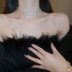 Detail view of luxury sparkling diamond necklace and bracelet on a model wearing black feathers