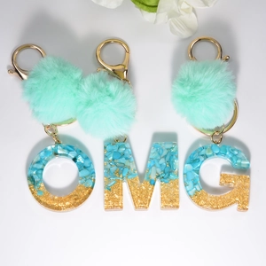 Close-up of O M G resin letters with mint green pompom and gold lobster clasp