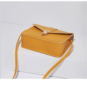 Detail of yellow rectangular crossbody bag with golden twist lock on white geometric base
