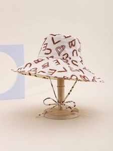 Detail of cream canvas sun hat with brown letter prints and decorative chin strap bow
