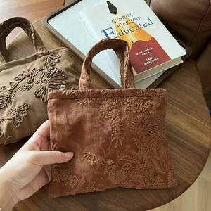 Close-up of vintage brown suede handbag featuring floral embroidery on a wooden tray