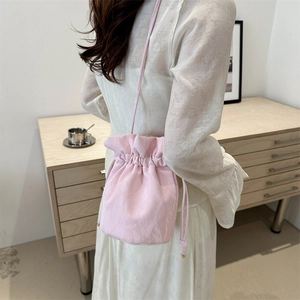 Chic pink drawstring bucket bag with pleated texture worn as a crossbody on model