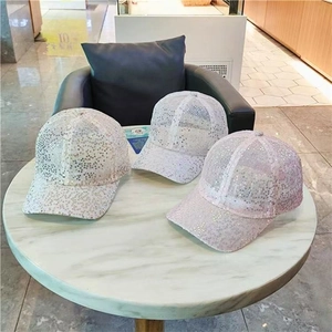 Detail of white, beige, and light pink sequin baseball caps on marble table background