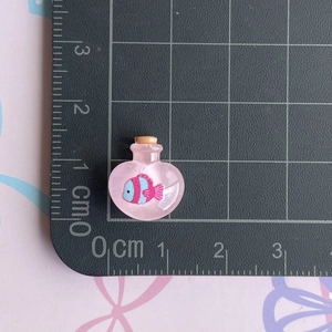 Macro view of a 1.5cm heart-shaped resin bottle charm with tiny fish inside on a scale mat