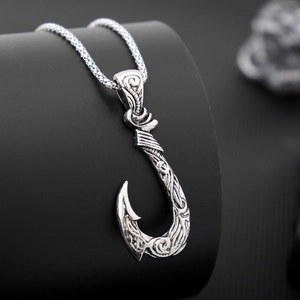 Macro shot of silver metal fish hook pendant with detailed engraved textures and finish