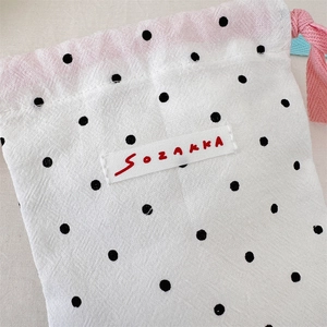 Detail of white cotton drawstring bag with black polka dots and pink ribbon closure