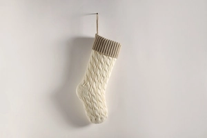 Detail of a cream white knitted Christmas stocking with classic cable pattern and hanging loop