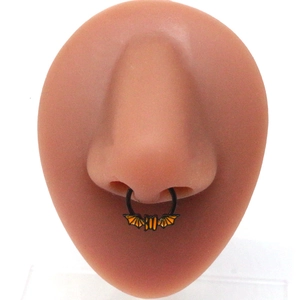 Detail view of black metal septum ring featuring a black bat with orange wings on nose model