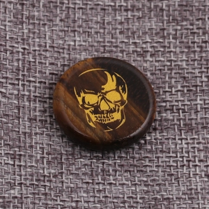 Detailed view of round tiger eye stone disc with a golden skull engraving on woven texture