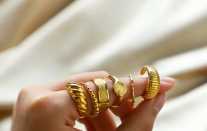 Detail of five stackable gold stainless steel rings on hand with silk background