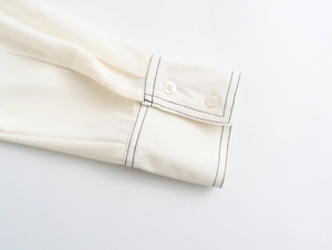 Detailed macro view of cream chiffon shirt cuff featuring black contrast stitching and buttons