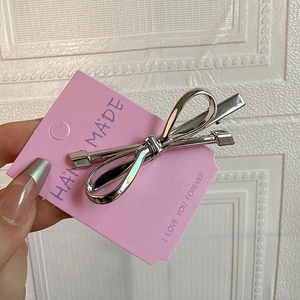 Close-up of a silver bow hair clip with polished metal finish on a pink display card