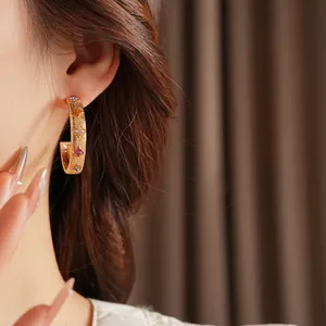 Golden brushed C-shaped hoop earrings with colorful gemstone flowers worn by a model