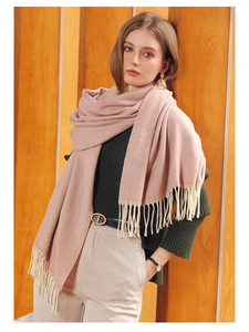 Close-up of pink herringbone scarf with tassels worn by model on green sweater