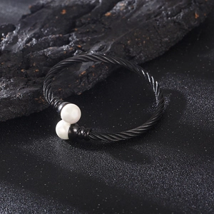 Detail of black twisted cable bracelet featuring two white pearls on a dark stone surface