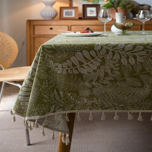 Macro detail of grass green linen tablecloth featuring white leaf prints and cream tassels